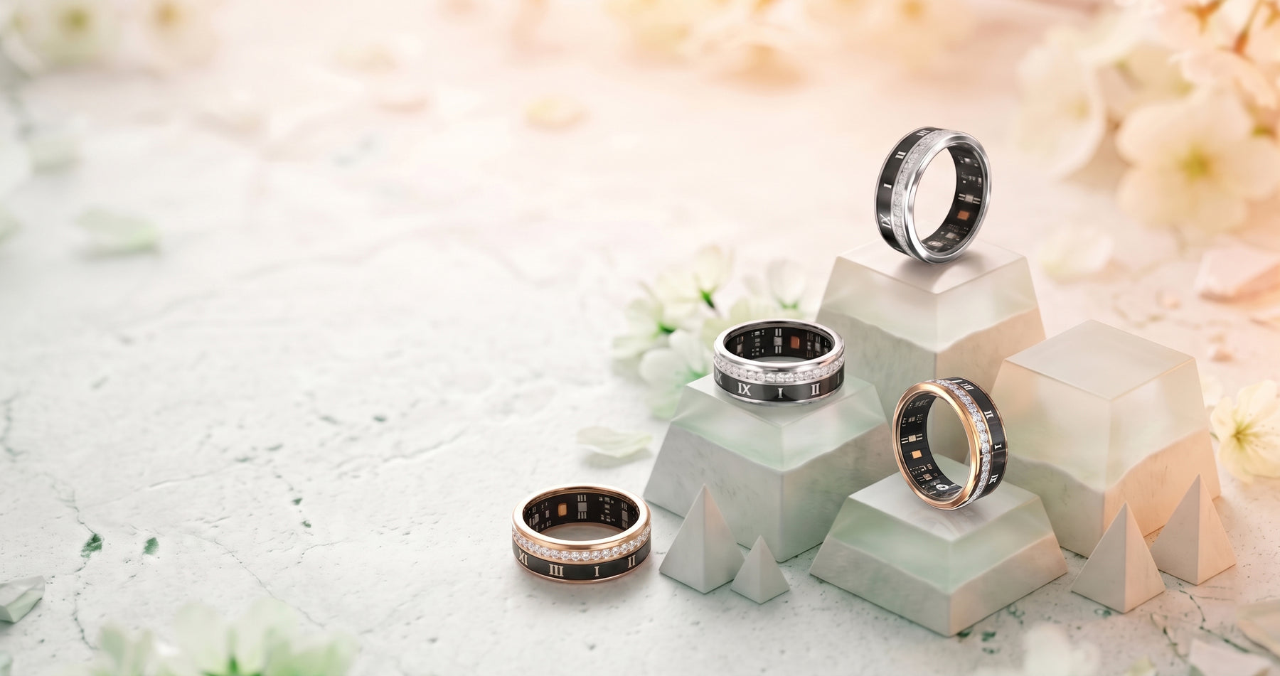 Three Luna smart rings in rose gold, silver and black, resting on pale stone blocks among white blossom.